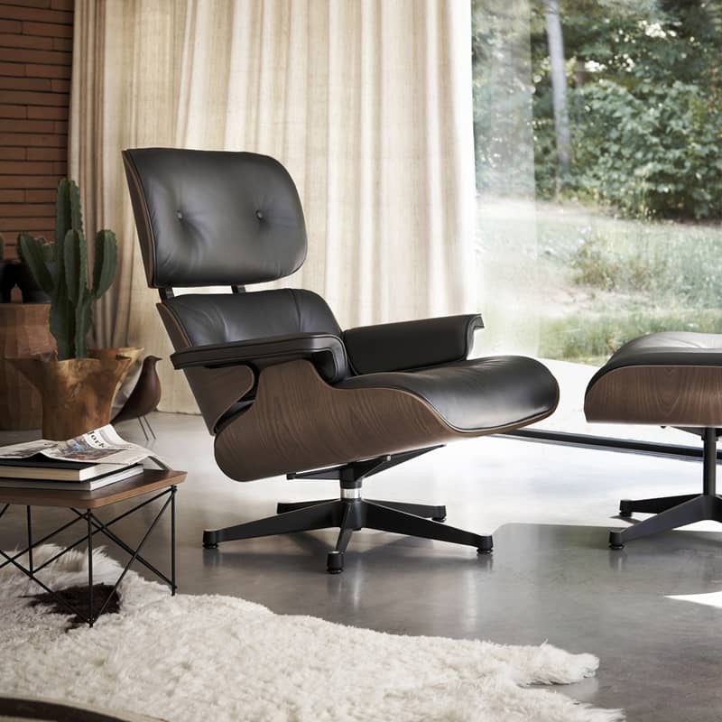 Der klassische Ledersessel Eames Lounge Chair steht in einem kuschelig eingerichteten Wohnzimmer mit Teppich und Vorh&auml;ngen